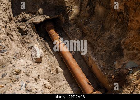 Das Loch wurde gegraben, um das Rohr zu reparieren und den Hahn auszutauschen. Abwassergraben mit Rohren Stockfoto