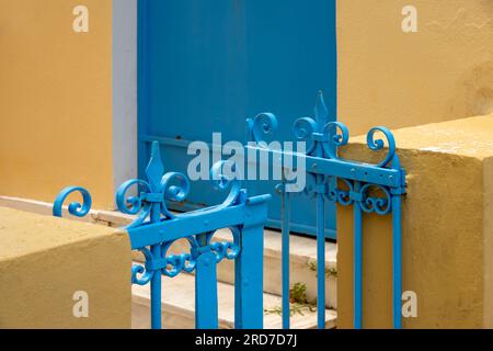 Zwei schmiedeeiserne und blau lackierte Gartentore aus Stahl zwischen Betonsäulen mit einer blauen Tür im Hintergrund Stockfoto