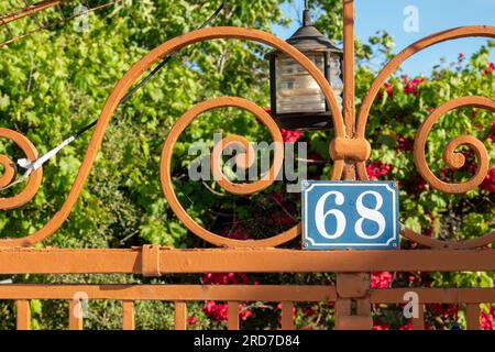 Schmiedeeiserne und lackierte Gartentore aus Stahl mit Büschen und Lampe im Hintergrund und einem Schild mit der Nummer 68 Emaille weiß auf blau Stockfoto