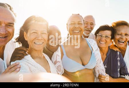 Glückliche Senioren, die bei Sonnenuntergang Selfie am Strand machen, während sie Sommerkleidung tragen - fröhlicher Lebensstil, Urlaub und Reisebegleitung Stockfoto