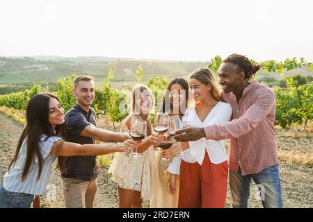 Fröhliche Freunde jubeln bei einer Sommerveranstaltung auf dem Land mit Rotwein - Multirassenfreunde haben Spaß während der kulinarischen Tour - Reisen, Urlaub und Sport Stockfoto