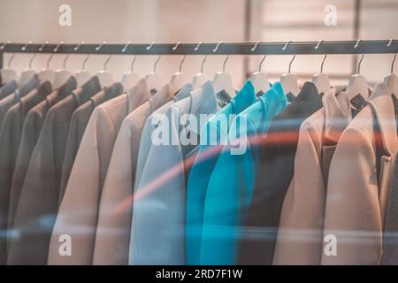 Elegante, legere Mäntel, die im Kleidergeschäft am Kleiderbügel hängen, verschwommenes Innenleben. Ladenkonzept, Verkauf Stockfoto