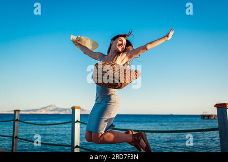 Junge Frau, die glücklich und frei auf dem Pier am Roten Meer springt. Spaß am Meer während der Sommerferien Stockfoto