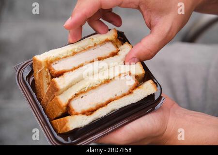 Eine unbekannte Person, die Katsu-Sando auf der Straße isst. Stockfoto