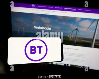 Person, die ein Mobiltelefon mit dem Logo des britischen Telekommunikationsunternehmens BT Group plc auf dem Bildschirm vor der Webseite hält. Konzentrieren Sie sich auf das Display des Telefons. Stockfoto