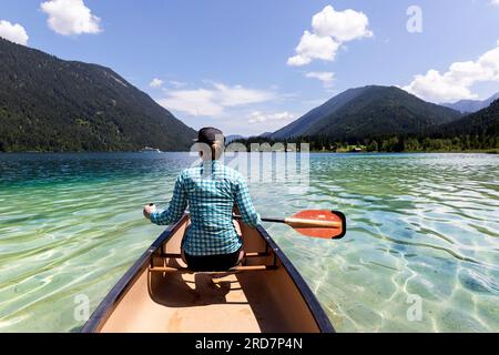 Frau Touristin paddelt in einem Kanu auf einem spektakulären Weissensee in Kärnten in Österreich, karibisches Wasser an einem schönen sonnigen Sommertag Stockfoto