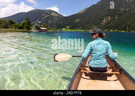 Frau Touristin paddelt in einem Kanu auf einem spektakulären Weissensee in Kärnten in Österreich, karibisches Wasser an einem schönen sonnigen Sommertag Stockfoto