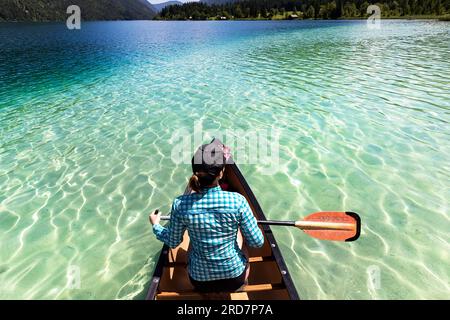 Frau Touristin paddelt in einem Kanu auf einem spektakulären Weissensee in Kärnten in Österreich, karibisches Wasser an einem schönen sonnigen Sommertag Stockfoto