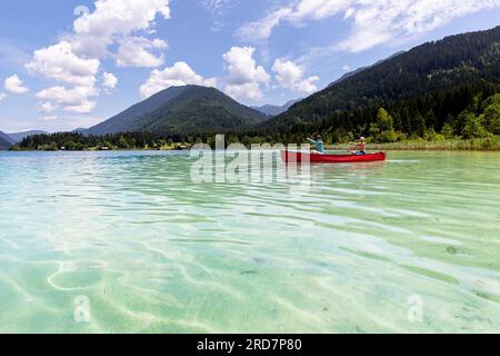 Mutter und Sohn paddeln im roten Kanu auf kristallklarem Wasser von Weissensee, Kärnten, Österreich, Europa Stockfoto