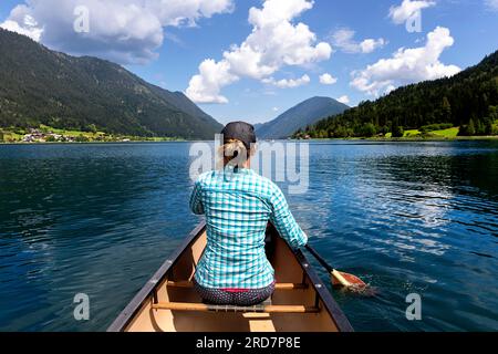 Frau Touristin paddelt in einem Kanu auf einem spektakulären Weissensee in Kärnten in Österreich, karibisches Wasser an einem schönen sonnigen Sommertag Stockfoto