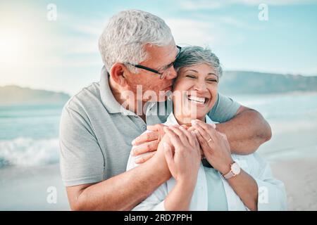 Glückliches, küssendes oder altes Paar, das am Strand mit Liebe, Pflege oder Unterstützung im Sommerurlaub in der Natur lacht. Ruhestand, reifer Mann, der sich umarmt, oder lustiger Senior Stockfoto
