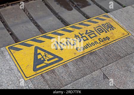 Gelb-schwarz gestreiftes Warnschild am Rand eines Bahnsteigs des Bahnhofs von Peking mit der Aufschrift „Achtung: Die Lücke“ auf Chinesisch. Stockfoto