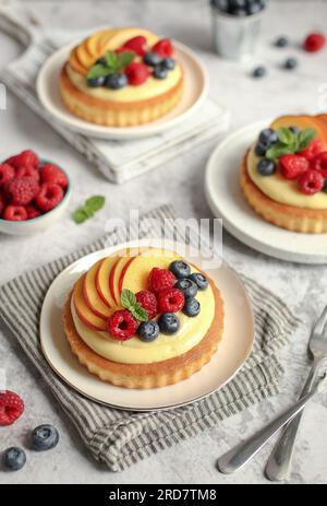 Weicher Obsttörtchen mit Vanillegebäck auf einem weißen Teller. Abgezogene Serviette und grauer Hintergrund. Stockfoto