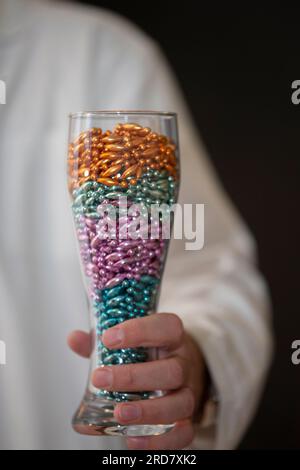 In seiner Hand ist ein langes Glas gefüllt mit mehrfarbigen Perlen. Stockfoto