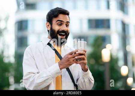 Ein glücklicher araber, der sein Smartphone benutzt, um im Freien tolle Nachrichten zu lesen Stockfoto