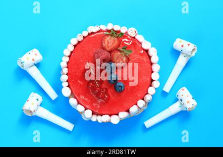 Beeren-Geburtstagskuchen auf blauem Hintergrund, Draufsicht. Kuchen und Hörner zum Geburtstag. Festlicher Kuchen Stockfoto