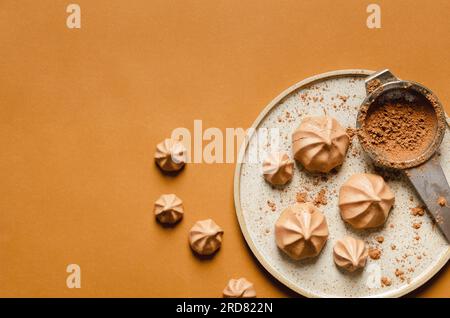 Schokoladen-Meringue-Kekse und Kakaopulver auf einem Teller auf braunem Hintergrund. Stockfoto