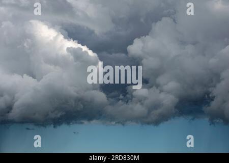 Bedrohliche Wolkenschichten bilden eine gerade Linie mit einem Streifen klaren Himmels, der einen dunkleren Regenstreifen zeigt. Stockfoto