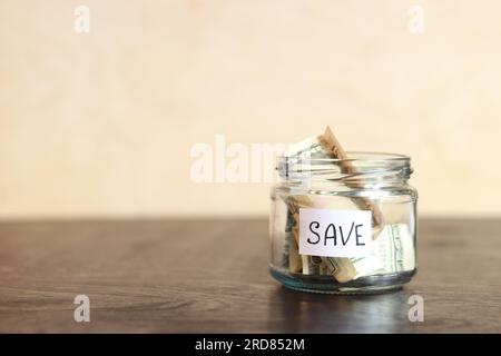Sparen Sie Geld für die Zukunft. Glasbehälter mit Dollars auf einem Holztisch. Sparschwein mit Banknoten, Kopierraum. Das Konzept der finanziellen Einsparungen Stockfoto