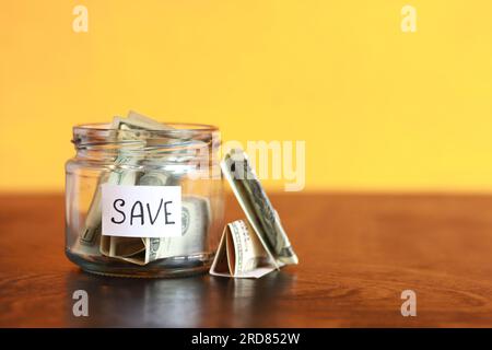 Sparen Sie Geld für die Zukunft. Glasbehälter mit Dollars auf einem Holztisch. Sparschwein mit Banknoten, Kopierraum. Das Konzept der finanziellen Einsparungen Stockfoto
