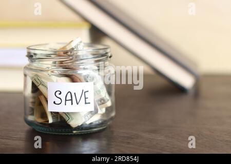Sparen Sie Geld für die Zukunft. Glasbehälter mit Dollars auf einem Holztisch auf dem Hintergrund von Büchern. Sparschwein mit Banknoten, Kopierraum. Das Konzept von Stockfoto