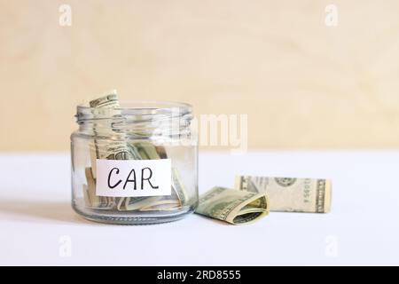 Ein Glasglas mit Dollarscheinen drinnen und daneben. Bank mit Geld-Nahaufnahme. Sparschwein mit Dollars für das Auto. Sparen Sie Geld für die Zukunft Stockfoto