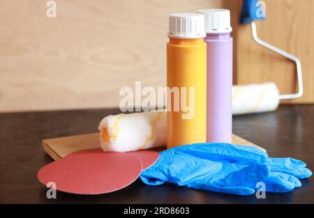 Zwei Flaschen Acrylfarbe auf einem Holztisch. Für die Reparatur benötigte Teile. Reparaturfarben, Gummihandschuhe, Schleifpapier und Holzbohlen. Platz für Text Stockfoto