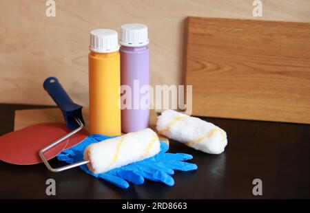 Zwei Flaschen Acrylfarbe auf einem Holztisch. Für die Reparatur benötigte Teile. Reparaturfarben, Gummihandschuhe, Schleifpapier und Holzbohlen Stockfoto