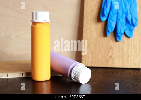 Zwei Flaschen Acrylfarbe auf einem Holztisch. Für die Reparatur benötigte Teile. Reparaturfarben und Gummihandschuhe Stockfoto