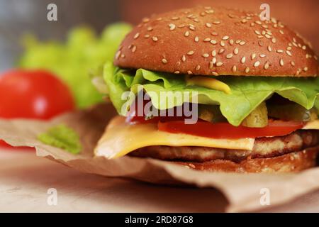 Cheeseburger auf einer Papierserviette-Nahaufnahme. Burger mit Hähnchenschnitzel, geschmolzenem Käse, Salat und Gemüse. Fastfood Stockfoto