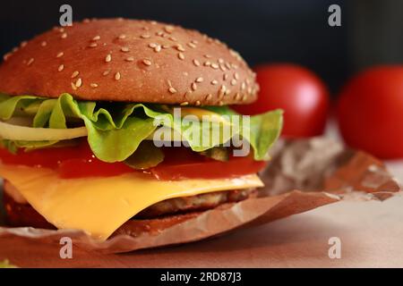 Köstlicher, saftiger Burger mit Kotelett und frischen Zutaten. Köstlicher Cheeseburger. Fast Food auf dunklem Hintergrund, Nahaufnahme Stockfoto