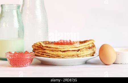 Ein Stapel dünner Pfannkuchen mit Kaviar auf hellem Hintergrund. Glasflasche mit Milch, Crepes, Kaviar und Ei. Stockfoto