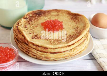 Pfannkuchen mit rotem Kaviar aus der Nahaufnahme auf dem Hintergrund des festlichen Tisches. Ein Stapel heiße Pfannkuchen. Maslenitsa, Shrovetide. Pfannkuchenwoche Stockfoto