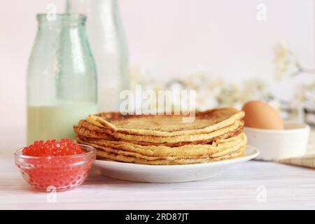 Stapel frisch gebackener Pfannkuchen liegen auf weißem Teller. Pfannkuchenwoche. Küche. Selektiver Fokus. Glasflasche mit Milch, Crepes, Kaviar und Ei Stockfoto