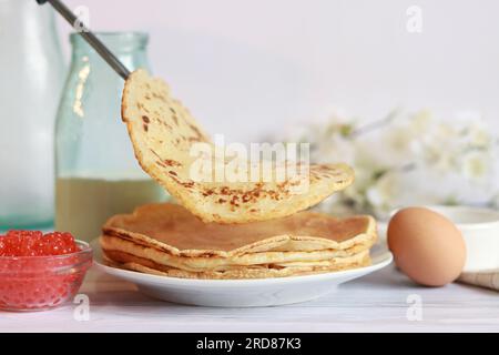 Ein Stapel heiße Pfannkuchen. Legen Sie neue Crepes auf einen Stapel fertig gebackener Pfannkuchen. Großer, runder, dünner Pfannkuchen. Pfannkuchenwoche. Maslenitsa Stockfoto