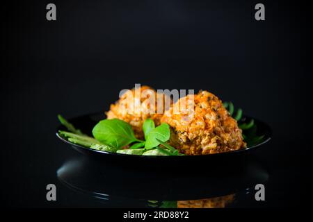 Gekochte Fleischbällchen auf einem Teller mit frischem Gemüse, isoliert auf schwarzem Hintergrund. Stockfoto