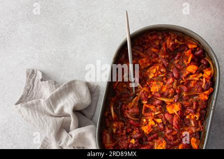 Gesundes Frühstück und Mittagessen, gedünstete rote Bohnen mit Karotten, Zwiebeln und Tomaten, Blick von oben auf eine ovale Keramikrösterei mit gedünsteten Hülsenfrüchten Stockfoto