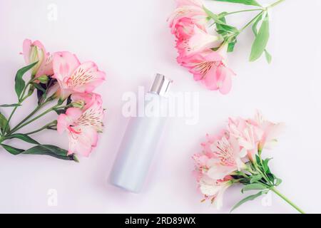 Blaue Kosmetikflasche und Alstroemeria Rosa Blumen auf weißem Hintergrund, flach liegend, Draufsicht. Leeres Label für Branding, Modell. Natürlicher ökologischer Kosmos Stockfoto