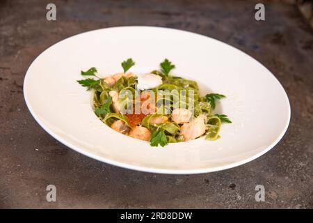 Grüne Pasta mit Lachs und rotem Kaviar und Grün auf einem weißen Teller. Stockfoto