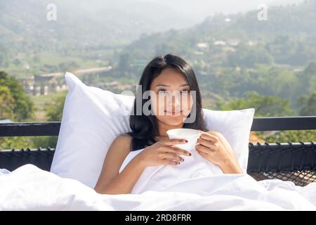 Eine junge Frau entspannt sich auf einer Veranda mit Blick auf ein Tal Stockfoto