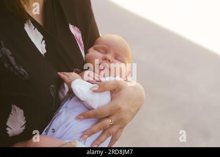 Mom wiegt ein Neugeborenes, das auf der Straße steht. Das Kind schläft in den Armen der Mutter Stockfoto