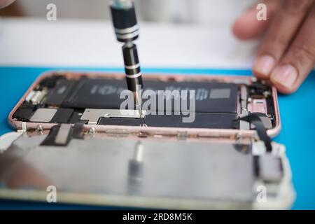 Nahaufnahme eines Reparaturwerkers, der das Smartphone wieder zusammensetzt, um die Batterie zu ersetzen Stockfoto