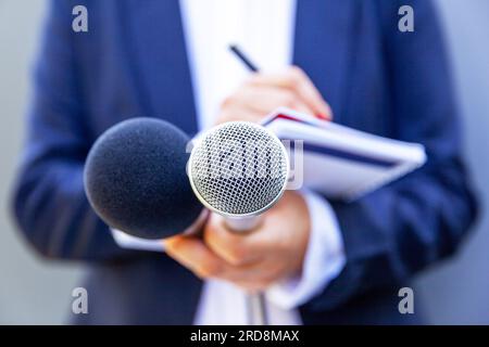 Weibliche Journalistin bei Pressekonferenz oder Medienveranstaltung, schreibt Notizen und hält Mikrofon Stockfoto