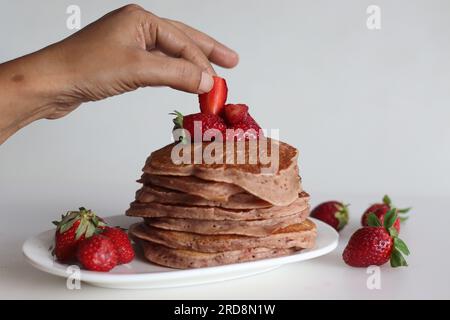 Buttermilch-Erdbeerpfannkuchen. Eine fruchtige Version von Pfannkuchen mit Erdbeersauce und frisch geschnittenen Erdbeeren, die dem Pfannkuchenteig hinzugefügt werden. Auf Whi geschossen Stockfoto