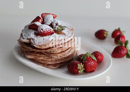 Buttermilch-Erdbeerpfannkuchen mit Zuckerpulver überzogen. Eine fruchtige Version von Pfannkuchen mit Erdbeersauce und frisch geschnittenen Erdbeeren Stockfoto