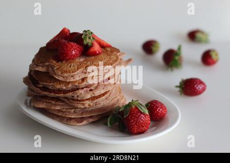 Buttermilch-Erdbeerpfannkuchen. Eine fröhliche Version von Pfannkuchen mit Erdbeersauce und frisch geschnittenen Erdbeeren, die dem Pfannkuchenteig hinzugefügt wurden. Auf Peitsche geschossen Stockfoto