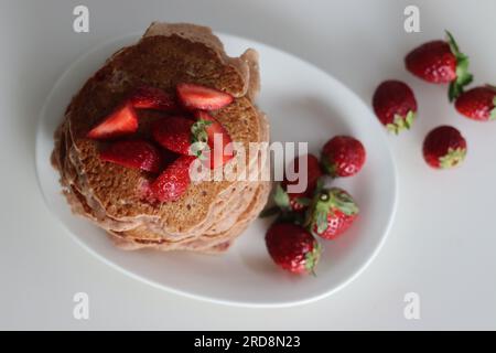 Buttermilch-Erdbeerpfannkuchen. Eine fruchtige Version von Pfannkuchen mit Erdbeersauce und frisch geschnittenen Erdbeeren, die dem Pfannkuchenteig hinzugefügt werden. Auf Whi geschossen Stockfoto