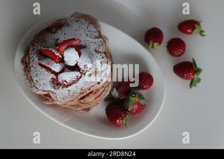 Buttermilch-Erdbeerpfannkuchen mit Zuckerpulver überzogen. Eine fruchtige Version von Pfannkuchen mit Erdbeersauce und frisch geschnittenen Erdbeeren Stockfoto