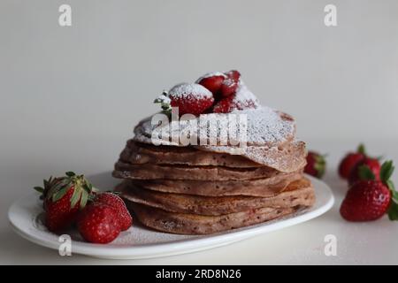 Buttermilch-Erdbeerpfannkuchen mit Zuckerpulver überzogen. Eine fruchtige Version von Pfannkuchen mit Erdbeersauce und frisch geschnittenen Erdbeeren Stockfoto