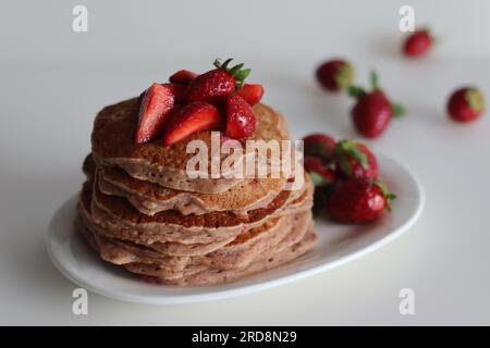 Buttermilch-Erdbeerpfannkuchen. Eine fruchtige Version von Pfannkuchen mit Erdbeersauce und frisch geschnittenen Erdbeeren, die dem Pfannkuchenteig hinzugefügt werden. Auf Whi geschossen Stockfoto